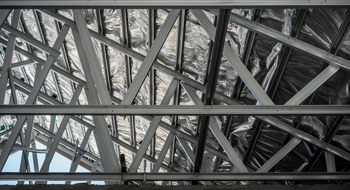 Image depicts an eExposed steel roof truss framework under a partly cloudy sky, showcasing modern construction techniques.